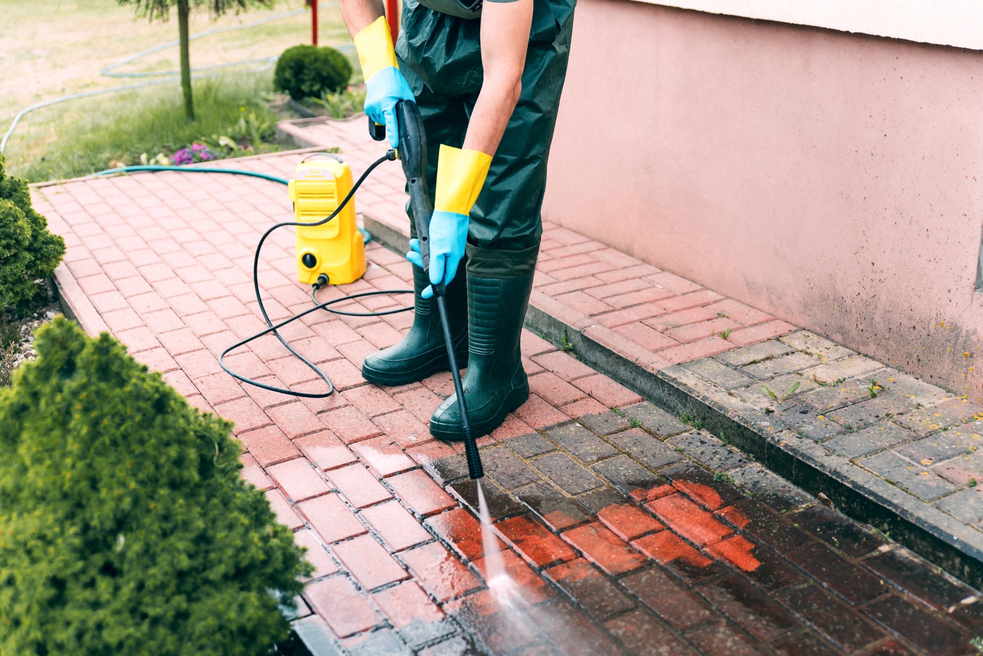 Man cleaning red, conrete pavement block using high pressure water cleaner. Paving cleaning concept